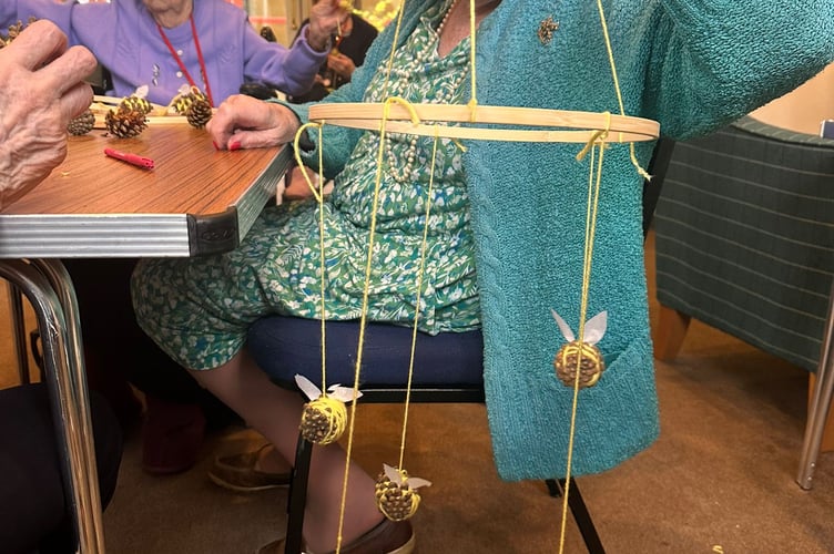 Resident Joan Edgley shows her handmade bee-decorated mobile, made of wood, string and pinecones