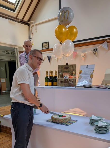 Seymours cuts the birthday cake at Haslemere Museum’s centenary celebration, with complimentary slices enjoyed by visitors.